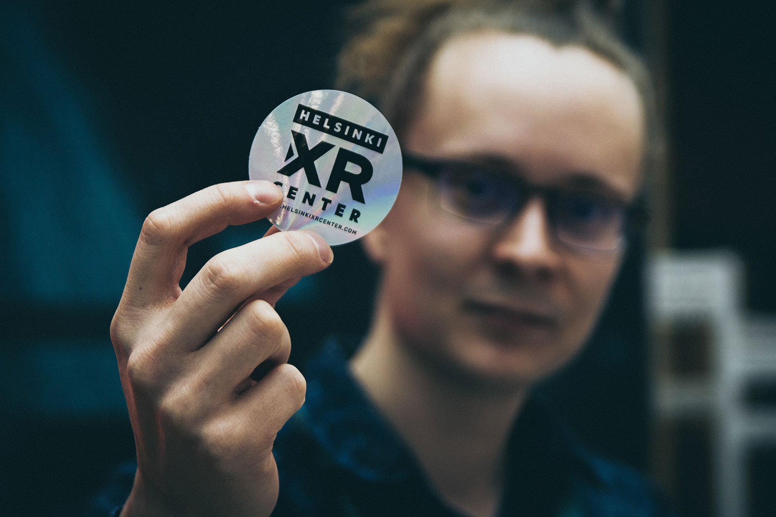 Helsinki XR Center crew member holding a HXRC sticker in the air.