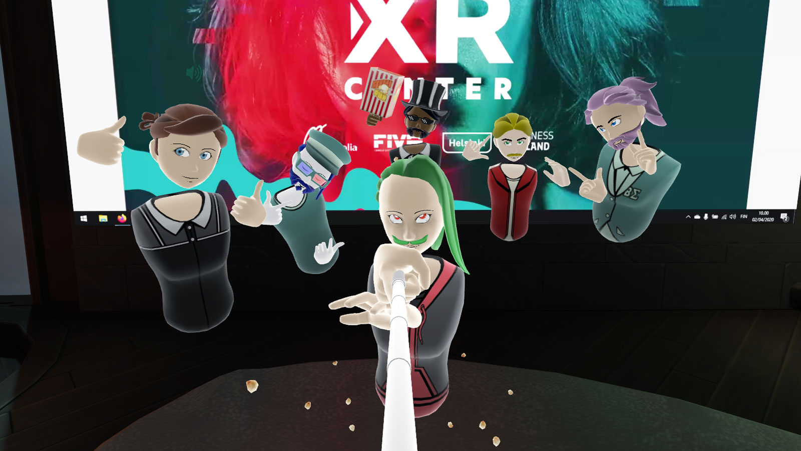 A screenshot of Bigscreen VR taken with a selfie stick. In the picture is six participants, the whole Helsinki XR Center crew, posing and smiling at the camera. Helsinki XR Center logo is on the screen in the background.