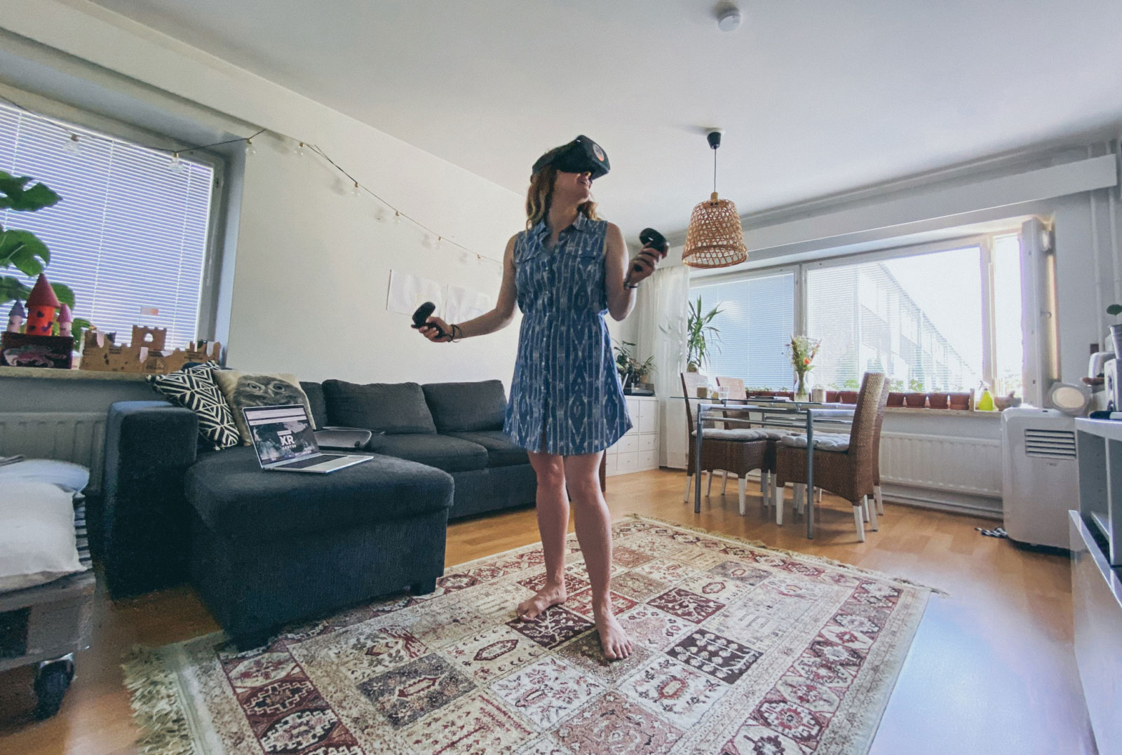 Woman at home, in the middle of a living room, using an Oculus Quest headset.