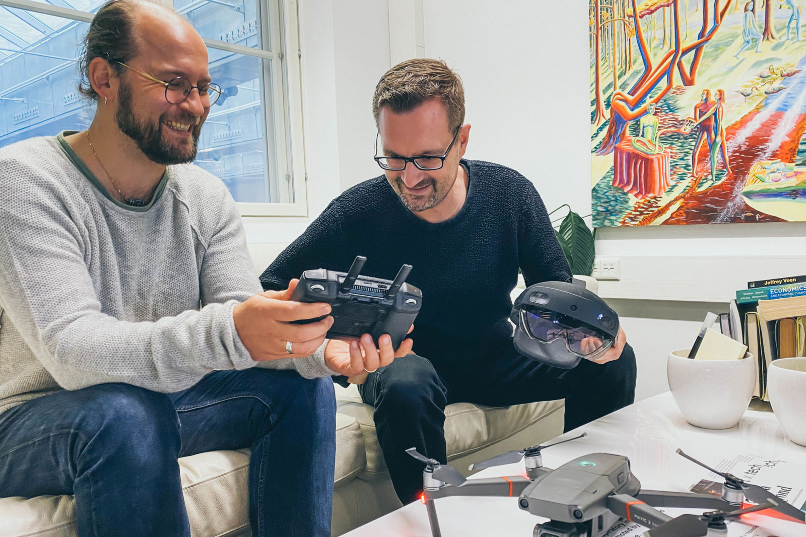 Lassi Immonen and Hannu Lesonen from Anarky Labs examining drone controllers. Both are wearing glasses, solid-coloured clothes, and are smiling.