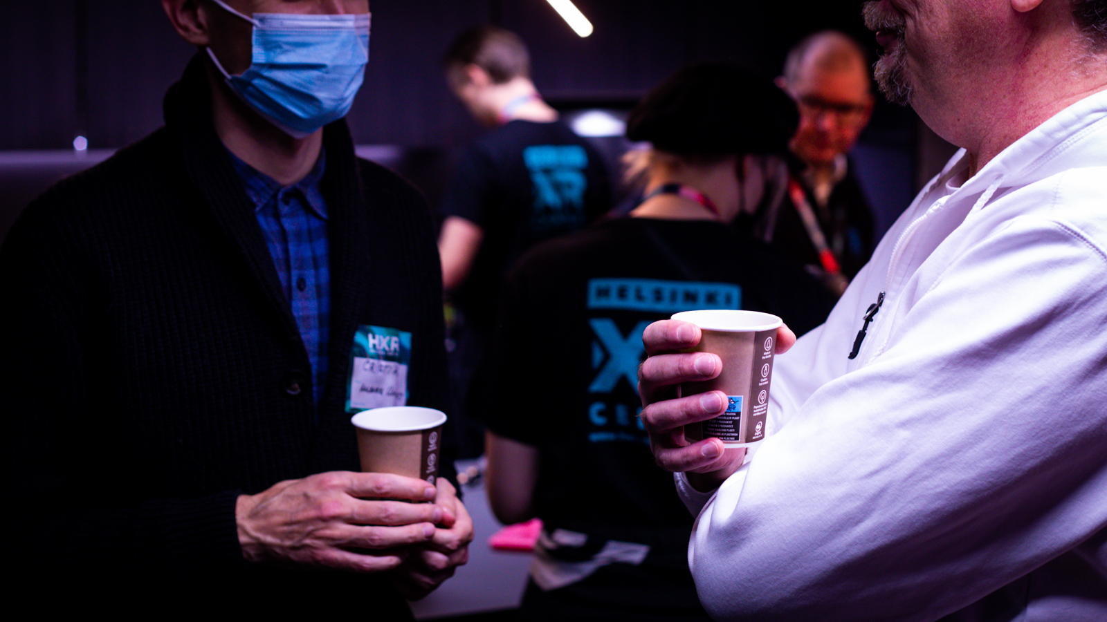 Two people talking at an event, with a zoom on their hands holding paper cups.