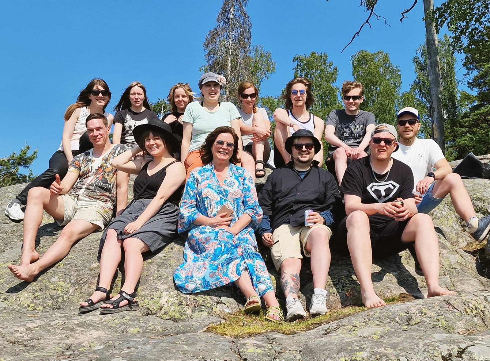 A group photo of 13 Helsinki XR Center team members sitting on a rock and smiling at the camera.