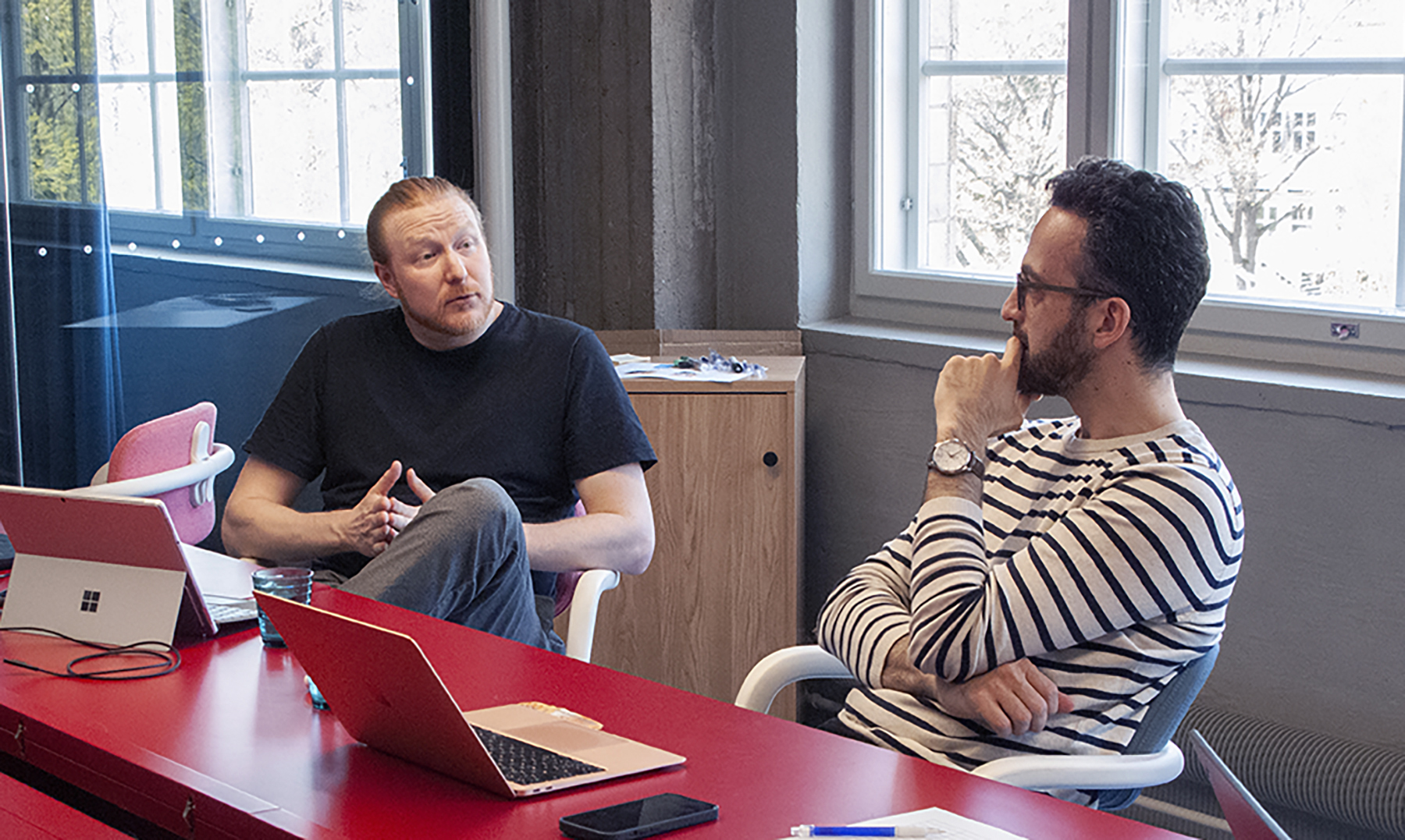 Coaches of HXRC Accelerator, Oki Tåg and Pouria Kay, are discussing at the last accelerator day. They are sitting on chairs in front of a big red table.